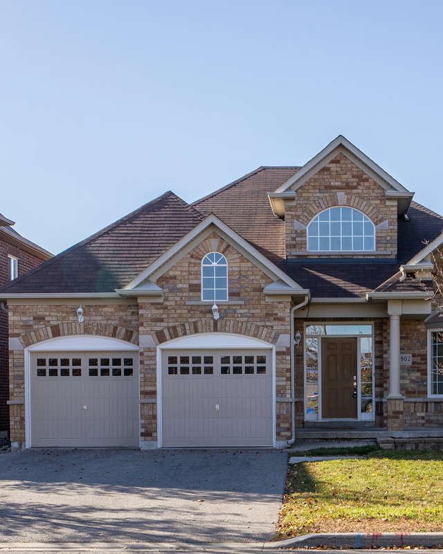 Front elevation of a detached brick and stone home with an arched window and a double garage